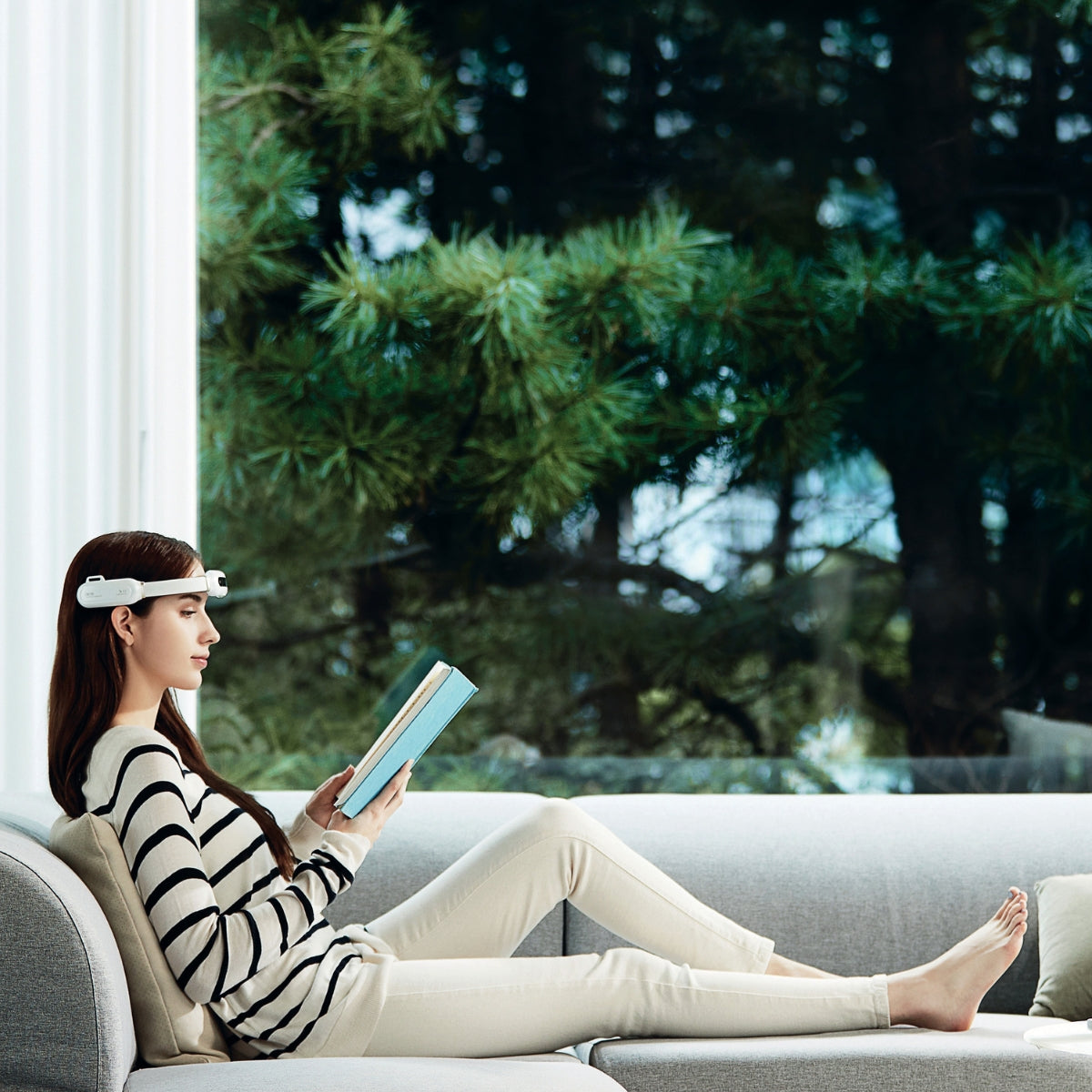 Frau sitzt ein Buch lesend auf dem Sofa. Sie trägt ein Herzion auf dem Kopf