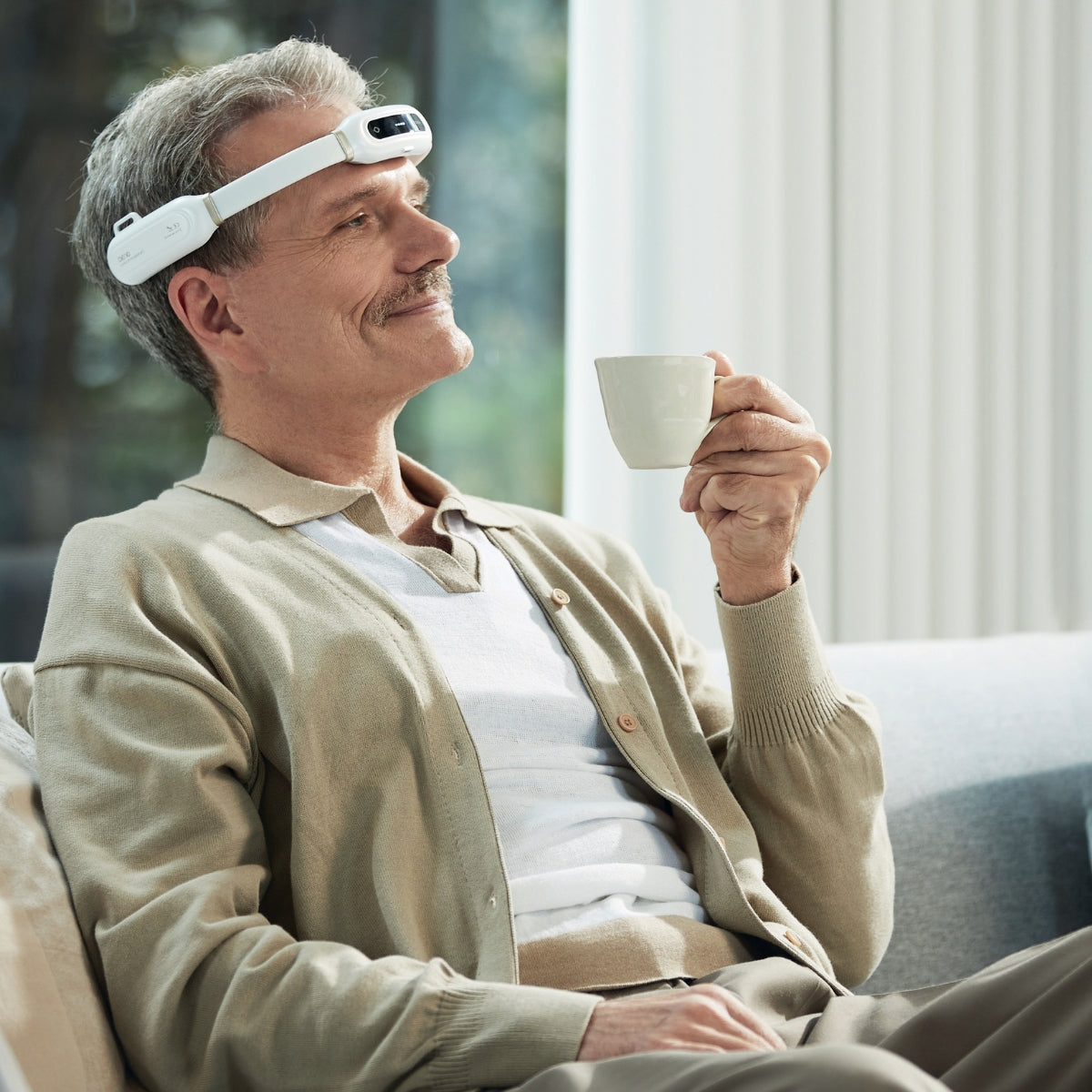 Mann sitzt mit einem Herzion auf der Stirn auf dem Sofa, während er eine Tasse Kaffee trinkt.