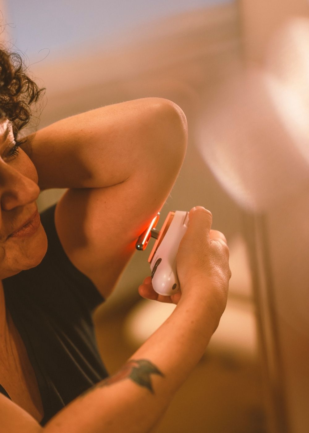 Frau hält sich Evosonics SoundWave Personal an den Oberarm um eine Lymphdrainage gegen schlaffe Oberarme mit Schallvibrationen und Rotlicht durchzuführen. | Therapiegold